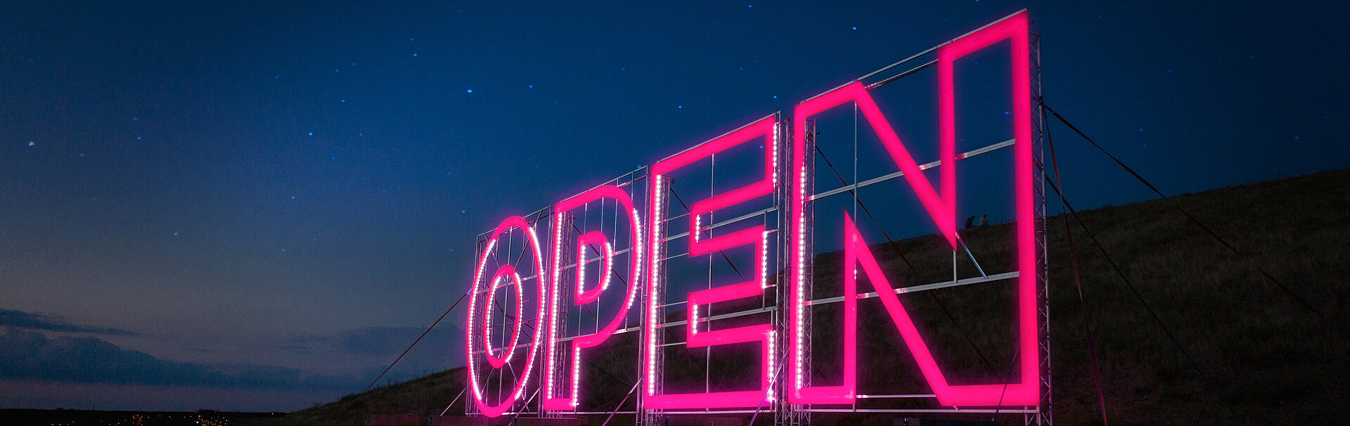 Pinker Leuchtschriftaufsteller mit dem Titel "OPEN", umgeben von Dunkelheit