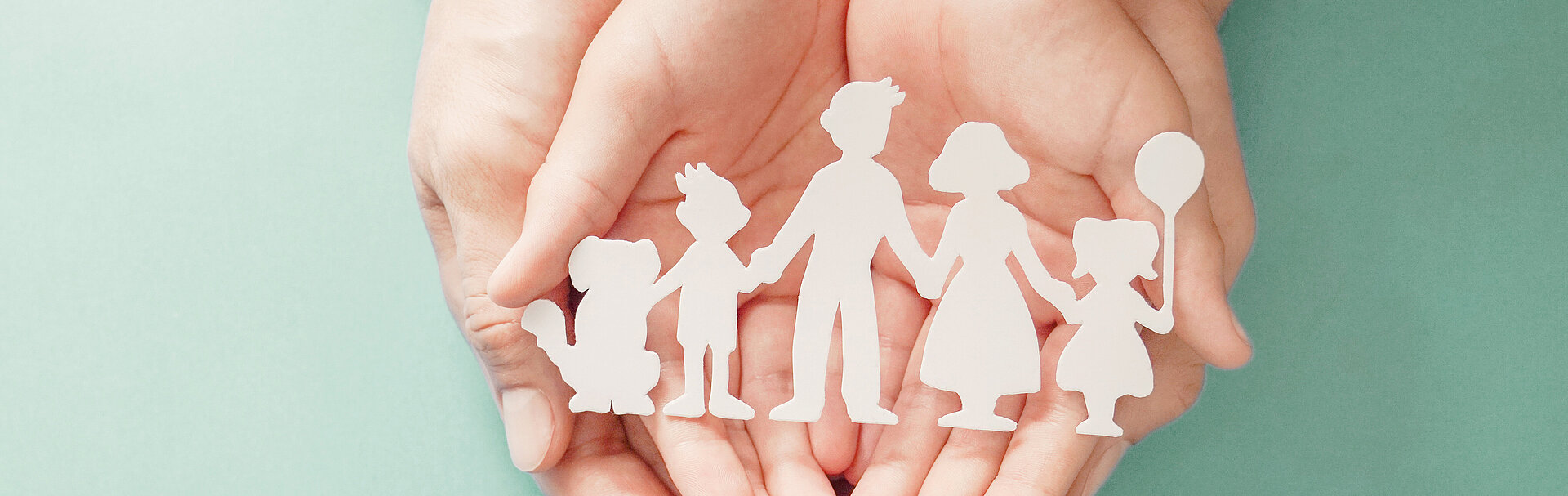 Eine offene menschliche Hand, mit einer Familienschablone (Hund, Kind, Vater, Mutter, Kind mit Ballon).